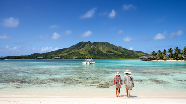 Lagon turquoise en Polynésie française pendant la saison sèche, avec plage de sable blanc, cocotiers et île verdoyante en arrière-plan