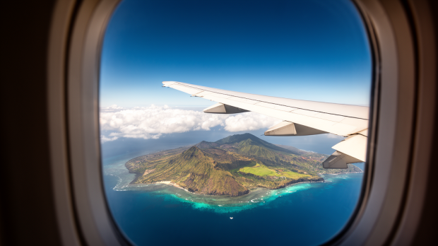 Vue réaliste depuis le hublot d’un avion long-courrier survolant La Réunion et son lagon turquoise.